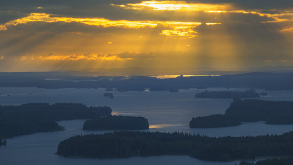 Aurinko paistaa järven yllä, pilvien raoista.