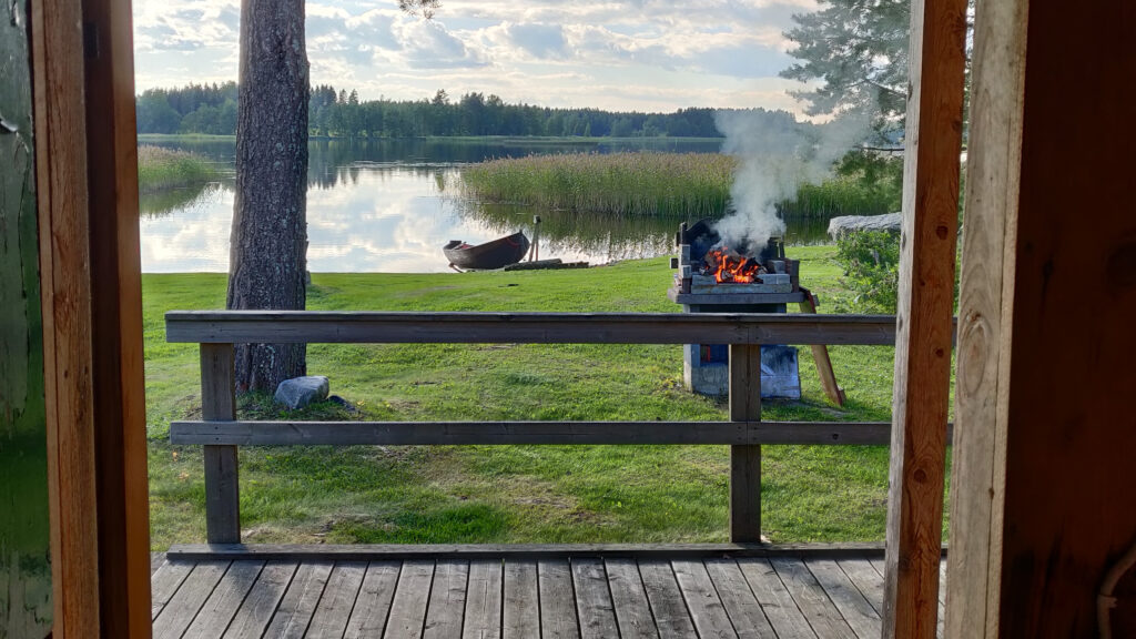 Kesäinen järvimaisema mökin pihasta, jossa näkyy grilli.