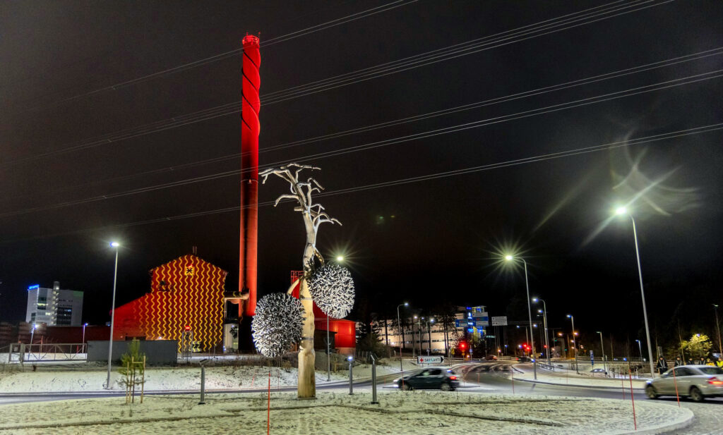 Yökuva, jossa kuvassa näkyvät kohteet, eli Savilahden kaukolämpökeskus ja liikenneympyrän taideteos Kauden satoa on valaistu hienosti.