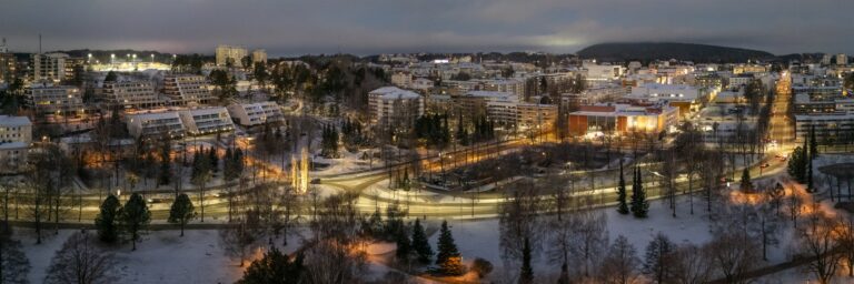 Iltahämärässä näkyvää kaupunkialuetta ja rakennuksia valaistuksineen.