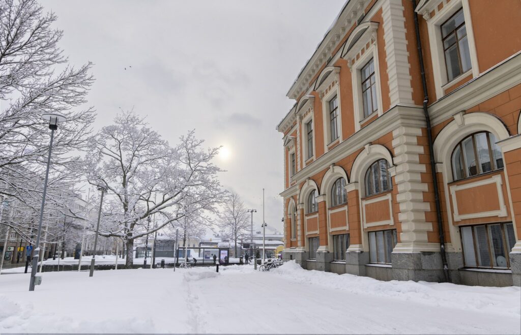 Talvinen maisema kaupungintalon laidalta. Oikealla kaupungintalo, vasemalla lumisia puita ja katu.