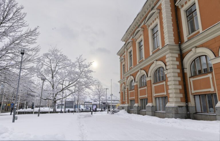 Talvinen maisema kaupungintalon laidalta. Oikealla kaupungintalo, vasemalla lumisia puita ja katu.