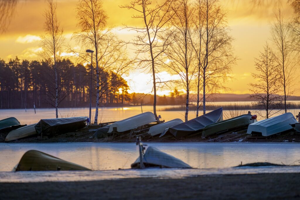 Talvinen rantamaisema auringonnousun aikaan. Rannalla veneitä talvisäilytyksessä.