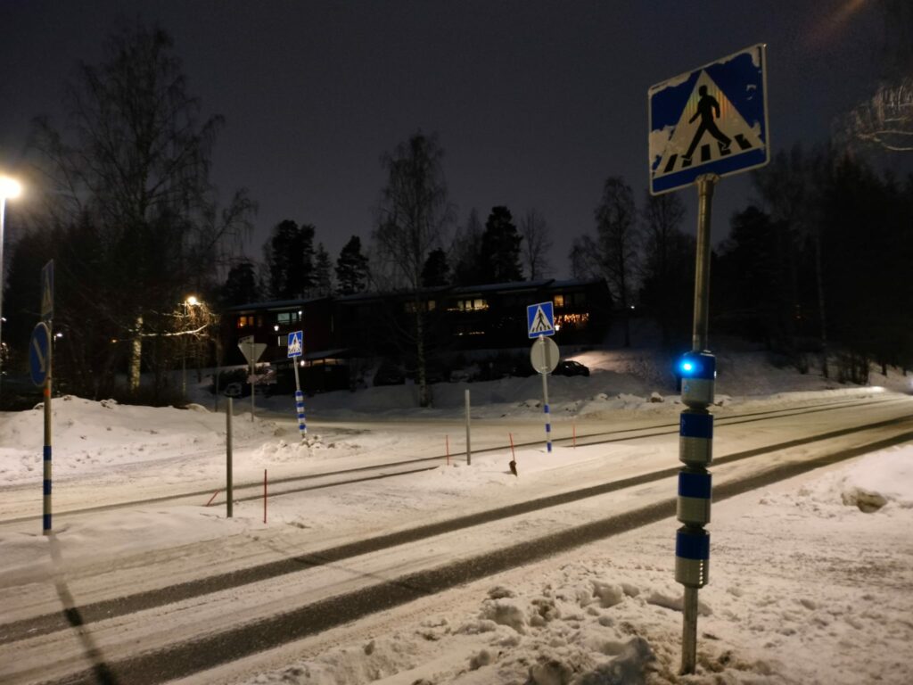 Pimeässä illassa näkyvä suojatievaroitin sekä lumista katua.