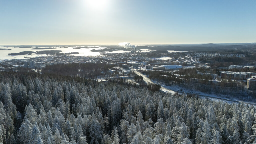 Talvinen ilmakuva, jossa taustalla sininen taivas, metsää ja kaupunkia.