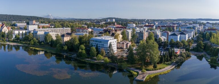 Kerrostaloja lammen rannalla kesäisenä, aurinkoisena päivänä.