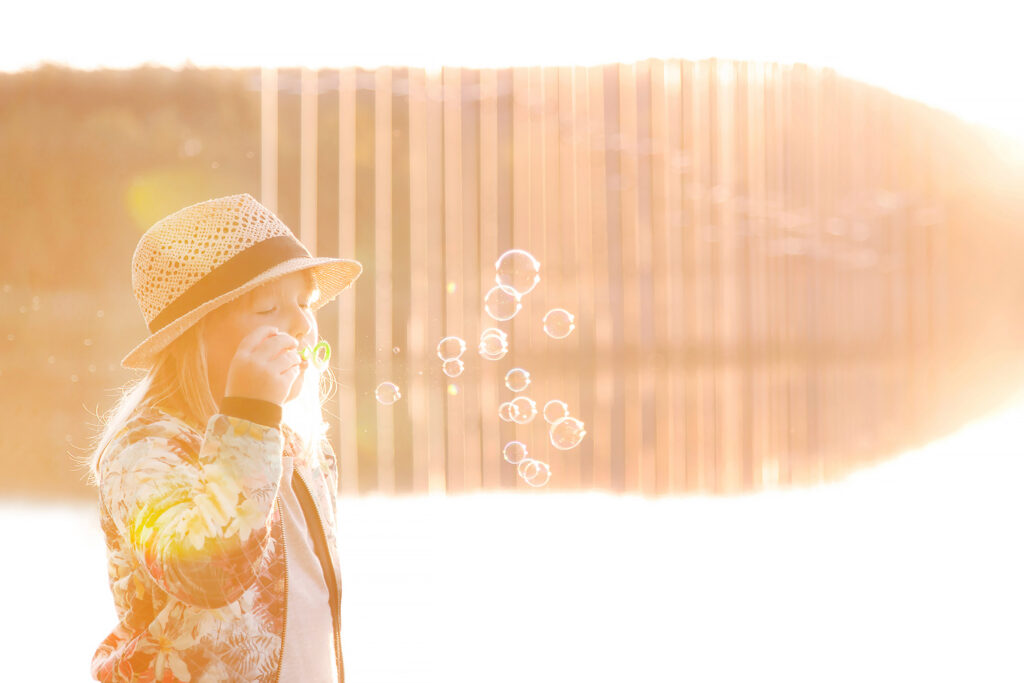 Tyttö puhaltaa saippuakuplia ilta-auringon valossa Savilahden rannalla.