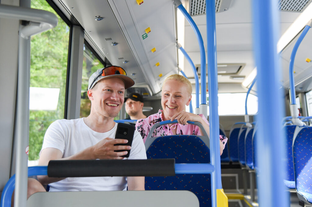 Kaksi henkilöä istuu iloisena bussissa.