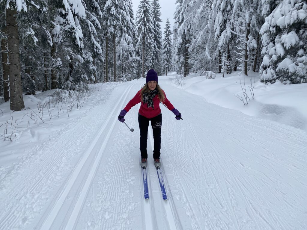 Punatakkinen nainen hiihtää perinteisellä hiihtoladulla talvisessa metsämaisemassa