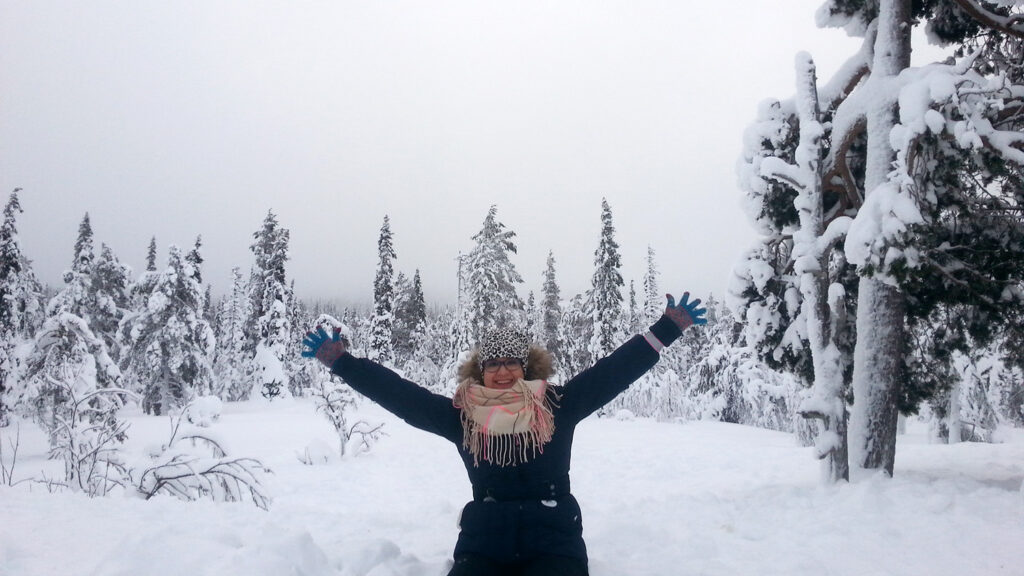 A woman is smiling with her arms raised in a winter landscape.