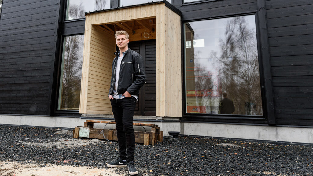 Young man stands in front of a modern balck house.