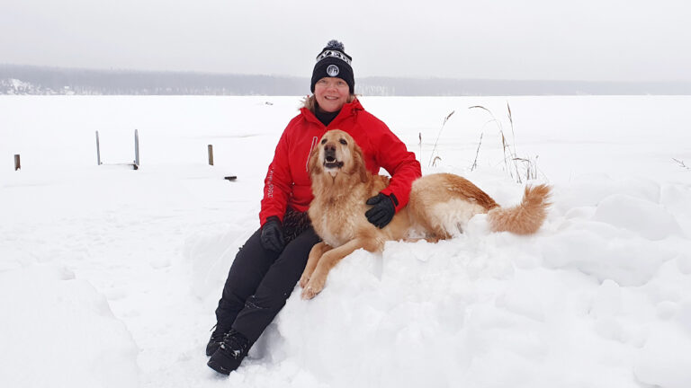 A woman is sitting on a snowbank with a dog.