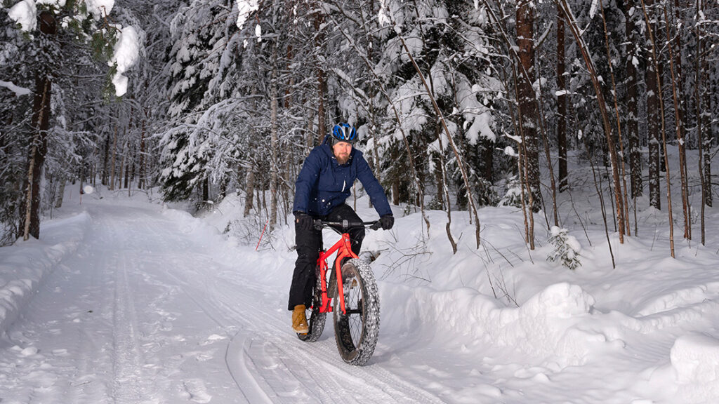 A man is cycling on a red mountain bike in a winter landscape.