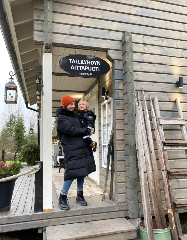 A woman is standing on the porch of an old building, holding a small child in her arms.