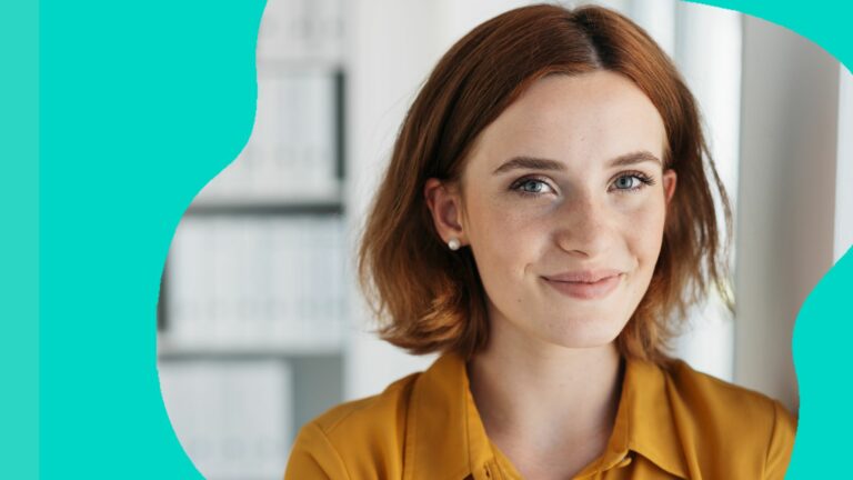 Attractive young businesswoman with a happy smile leaning against an office wall looking at the camera in a close up portrait